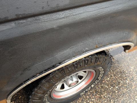 1989 Ford Bronco - A close-up shot focuses on the wheel well and tire of a vehicle, showing some rust and wear.
