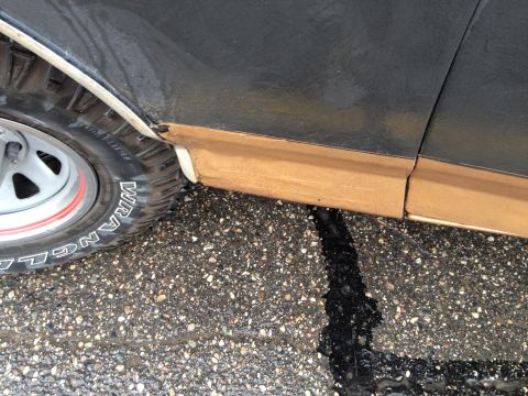 1989 Ford Bronco - A close-up view of the side panel and tire of a 1989 Ford Bronco on wet asphalt.