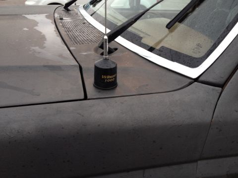 1989 Ford Bronco - Close-up of a Wilson 1000 antenna mounted on the hood of a dark-colored vehicle.