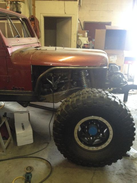 1985 Jeep CJ7 - A partially disassembled Jeep CJ sits in a workshop with a large off-road tire prominently displayed.