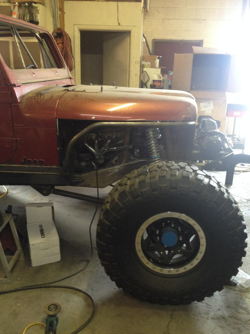 Red Jeep CJ with custom front end, large off-road tire, and exposed engine components