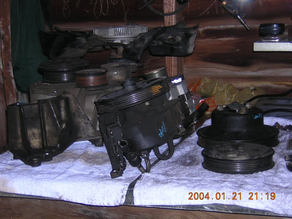 Assortment of black automotive parts, including power steering pumps and pulleys, laid out on a white towel