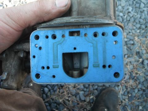 1972 International Scout II - Carburetor base plate with blue gasket, held for inspection.
