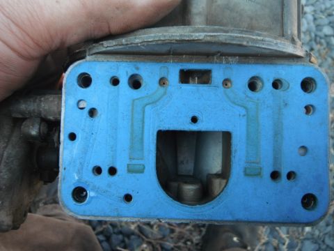 1972 International Scout II - Close-up of a carburetor base plate with a blue gasket, held by a hand.