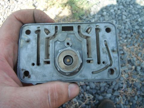 1972 International Scout II - Close-up of a carburetor base plate, held by a hand, with visible internal fuel passages.