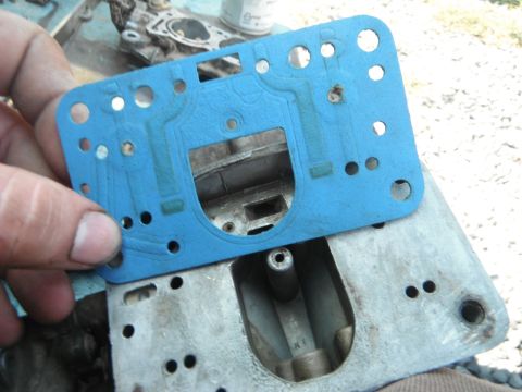 1972 International Scout II - A blue gasket is being held over a metal carburetor base, showing a close-up of engine parts.