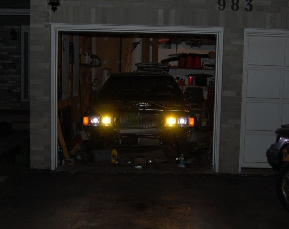 car with headlights on in a garage, house number 983 above door