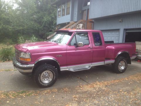 1992 Ford F-150 - A pink 1992 Ford F-150 pickup truck is shown from a three-quarter front angle in front of a house.