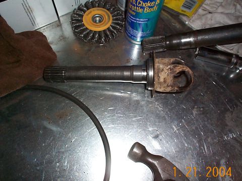 1992 Ford Bronco - A driveshaft U-joint assembly with splines and a rusty yoke is shown on a metal workbench next to tools and cleaning supplies.