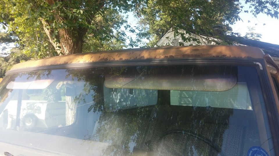 Rusted brown roofline above windshield of an old vehicle. Sun visors visible inside