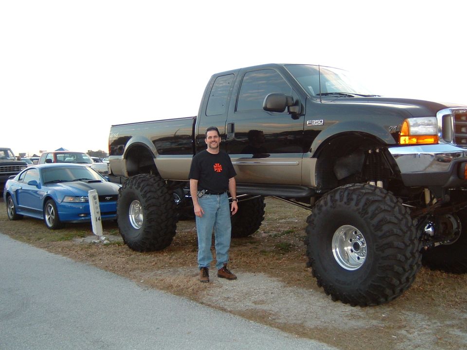 Man standing beside lifted black Ford F-250 Super Duty next to blue Mustang