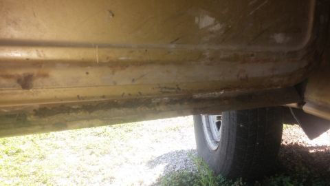 1979 Ford Bronco - Close-up of a vehicle's lower body panel reveals significant rust and dirt, with a tire visible.