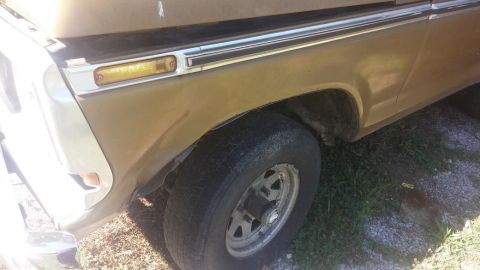 1979 Ford Bronco - Close-up of the front fender and wheel of a gold 1979 Ford Bronco, showing body damage.
