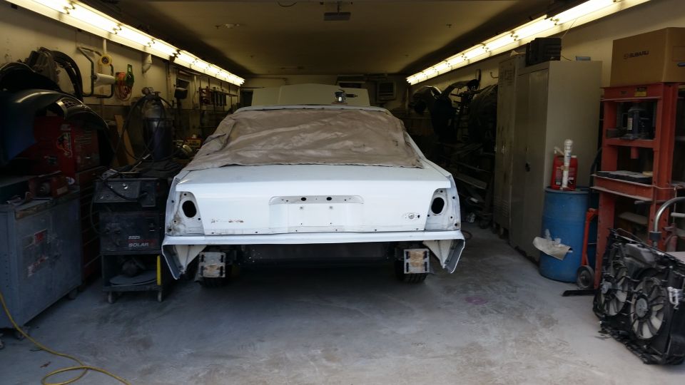 Rear view of a white sedan covered with a tarp in a workshop, undergoing repairs
