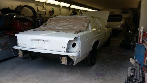 1991 Ford LTD Crown Victoria - A white sedan is undergoing repairs in a garage, with another vehicle parked behind it.
