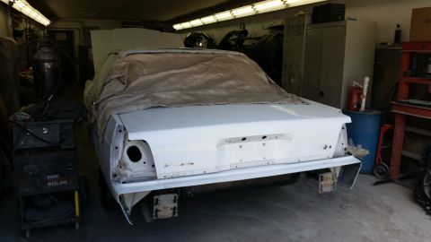 1991 Ford LTD Crown Victoria - A white sedan body is undergoing repairs in a garage, with its rear end exposed and parts removed.
