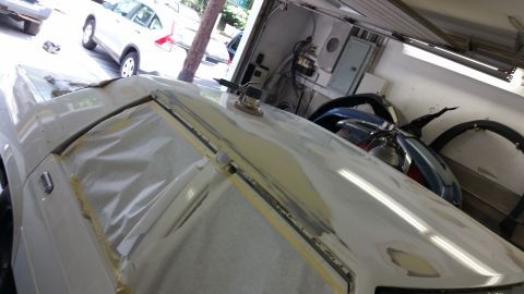 1991 Ford LTD Crown Victoria - A car's hood is covered in masking tape and primer, with a sanding tool resting on top, in a workshop setting.