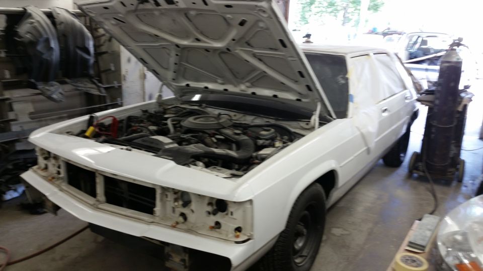 White sedan with hood open, showing engine bay. Grille is missing. Some body panels are covered with masking tape
