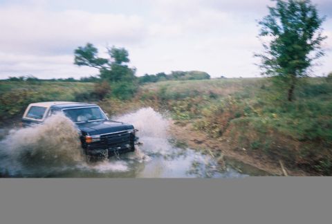 1991 Ford Bronco - A 1991 Ford Bronco navigates a muddy water crossing, sending a large spray of water into the air.