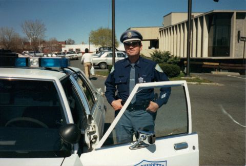 1991 Ford LTD Crown Victoria - A Massachusetts State Police officer stands by a 1991 Ford Crown Victoria LTD patrol car in a parking lot.