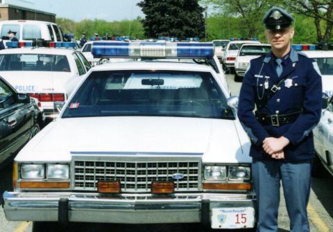 1991 Ford LTD Crown Victoria - A Massachusetts State Police officer stands next to a 1991 Ford Crown Victoria Police Interceptor, with other police vehicles in the backgr…