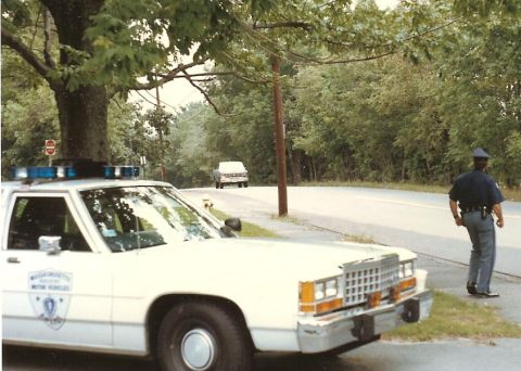 1991 Ford LTD Crown Victoria - A 1991 Ford Crown Victoria LTD police car is parked on the side of the road, with a state trooper standing nearby and another vehicle in th…