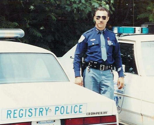 Police officer in uniform standing next to a 1991 Ford Crown Victoria LTD marked REGISTRY POLICE