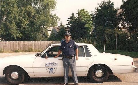 1991 Ford LTD Crown Victoria - A Massachusetts Registry of Motor Vehicles police officer stands beside a white 1991 Ford Crown Victoria LTD sedan.