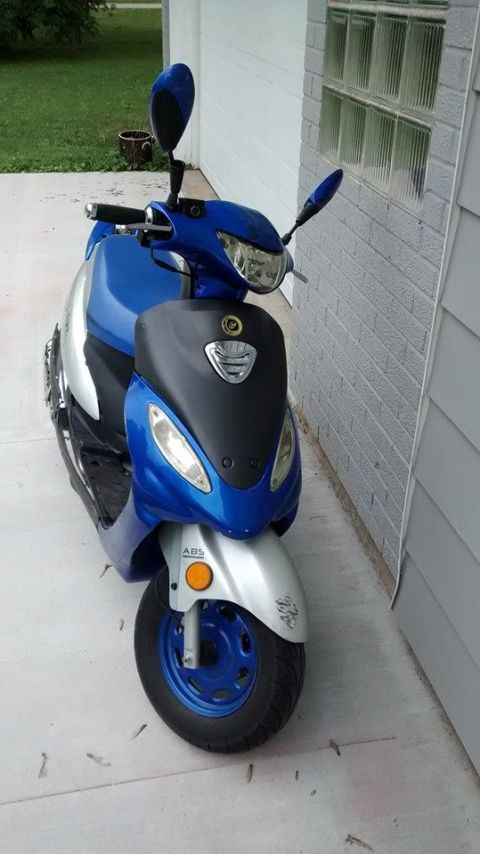 2006 Ford E350 - A blue and silver scooter is parked on a concrete driveway next to a building.