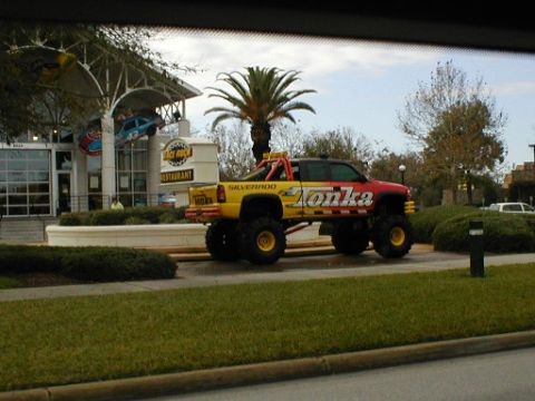 1979 Ford Bronco II - A custom monster truck painted in red and yellow Tonka colors is parked outside a restaurant.