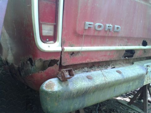 1978 Ford Bronco - The rear of a red Ford truck shows significant rust damage around the wheel well and bumper.