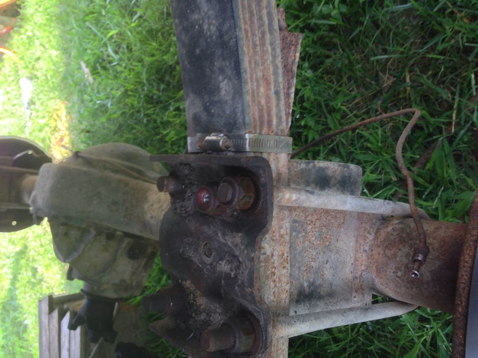 Close-up of a rusty rear axle with leaf springs and U-bolts. Some brake line is visible