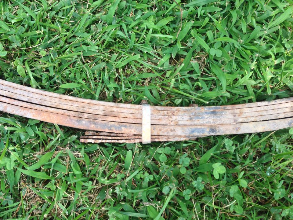 Rusty leaf spring with a metal band holding the leaves together, lying on grass