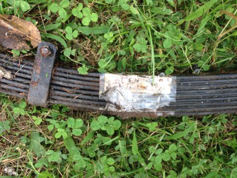 1979 Ford Bronco - A close-up view of a vehicle's leaf spring lying on the grass, with a piece of tape on it.
