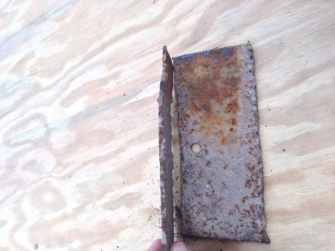 1979 Ford Bronco - A heavily rusted metal bracket is shown against a wood grain background.