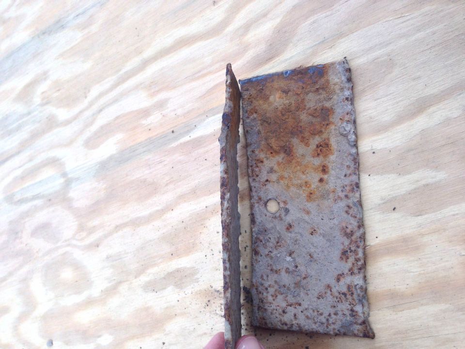 Rusted metal bracket with a bent edge, held by fingers against a wooden surface