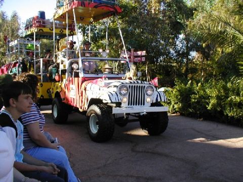 1979 Ford Bronco II - This modified Jeep CJ-7, adorned with animal print and carrying passengers in a safari-style carriage, is seen on a sunny day.