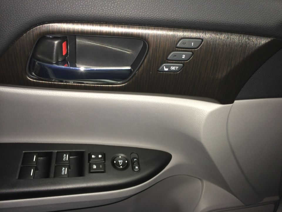 Car door panel with chrome handle, wood trim, window controls, and mirror adjustment. The panel is gray and black