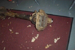 1996 Ford Bronco - A close-up view of a rusty front axle assembly, likely from an older vehicle, resting on a dark red mat.