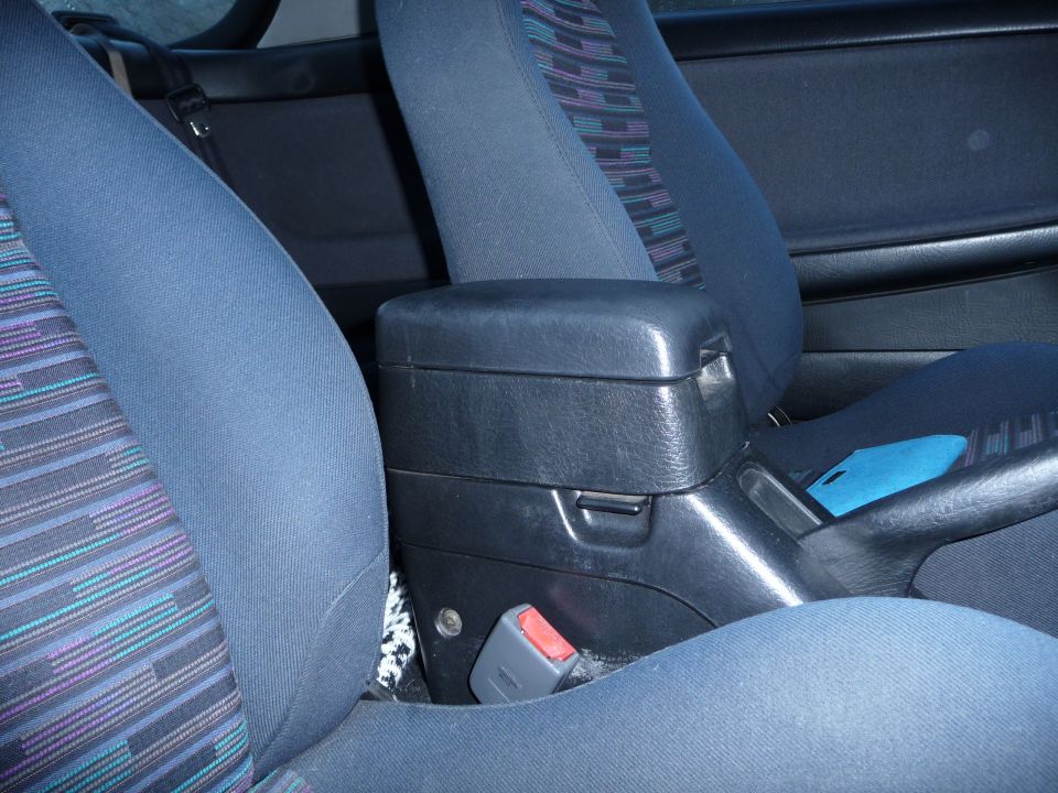 Car interior showing blue patterned seats, black center console with armrest, and seatbelt buckle