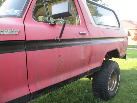 1979 Ford Bronco - The side of a red 1979 Ford Bronco Ranger with a black stripe and visible rust damage.