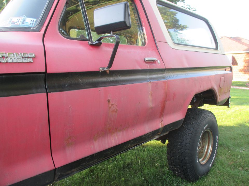 Red 1979 Ford Bronco Ranger side view, showing rust spots and a black stripe