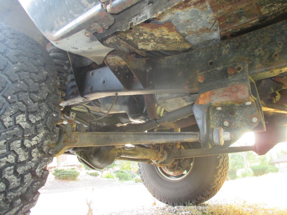 Underside view of a 4x4 vehicle's frame, suspension, and tires. Shows significant rust