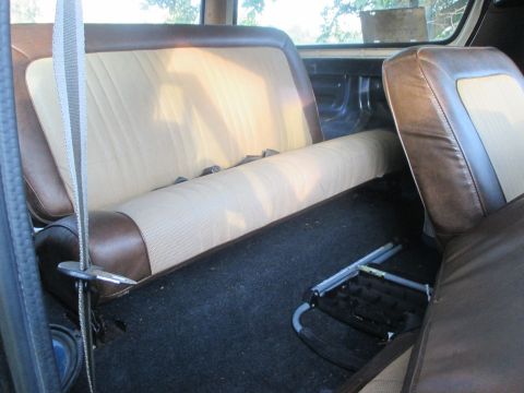 1979 Ford Bronco - The interior of a vehicle shows the rear bench seat and carpeting, with a detached seat frame on the floor.