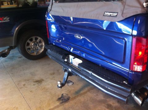 1982 Ford Bronco - A blue Ford Bronco with a soft top is parked next to a dark blue Ford F-series truck in a garage.