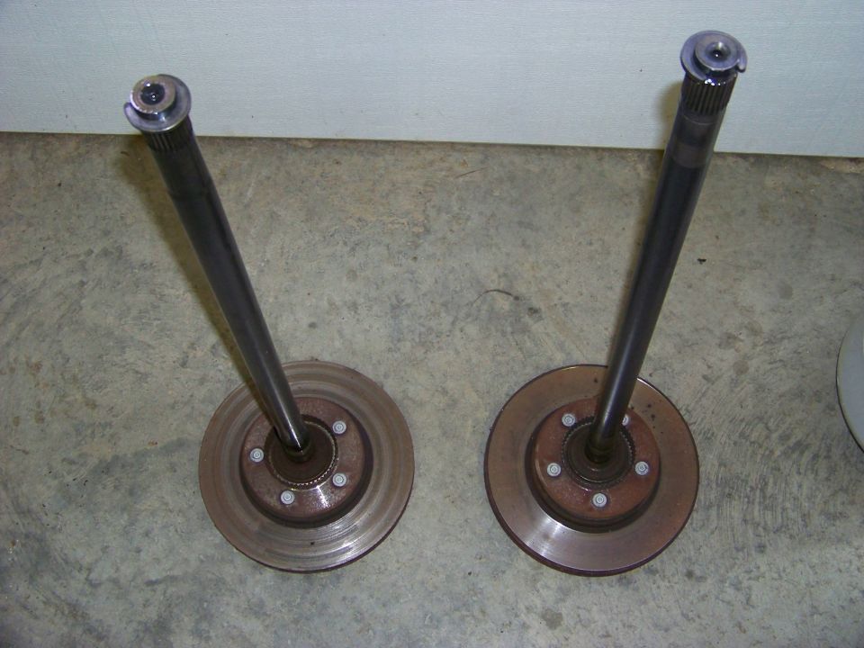 Two axle shafts with brake rotors attached, resting on a concrete floor