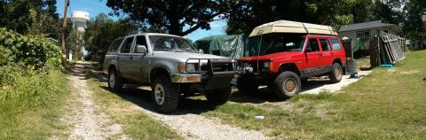 1986 Ford Bronco - Two SUVs, a silver Toyota 4Runner and a red Jeep Cherokee, are parked on a gravel driveway.