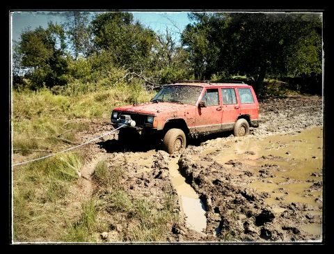 1986 Ford Bronco - This red Jeep Cherokee is stuck in a muddy trail, with a rope attached to the front winch.