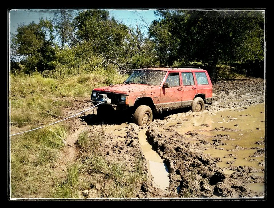 Red Jeep Cherokee stuck in deep mud, being pulled by a rope