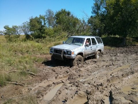 1986 Ford Bronco - A silver Toyota 4Runner navigates a muddy terrain, with its front end partially submerged in the mire.